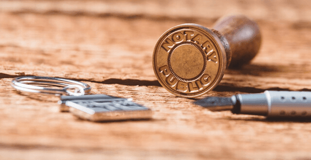 Notary public stamp and fountain pen on a wooden surface with a keychain nearby.